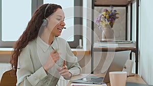 Young professional woman sales agent in headset with mic video chatting with client online via laptop, empty space