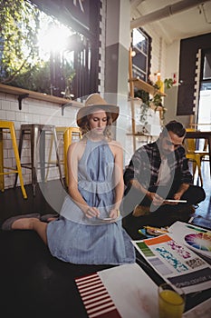 Young professionals using technologies while sitting with sheets on floor