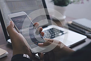 Young programmer writing program code sitting at the workplace with laptop and mobile phone in the office