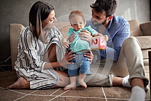 Young proud family playing and baby learning to walk at home