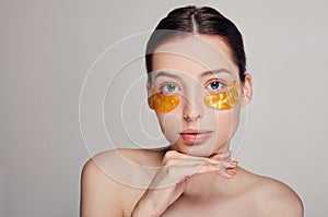 Young ptitty girl applying golden collagen patches under her eyes. Remove wrinkles and dark circles