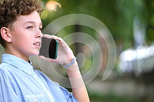 Young puzzled child boy talking on cellphone outdoors in summer park