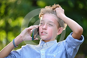 Young puzzled child boy talking on cellphone outdoors in summer park