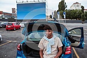 Young puzzled man in open car trunk at autocinema