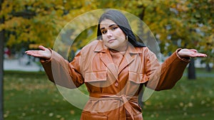 Young puzzled upset hispanic woman standing outdoors in park shrugging shoulders doubtful looking at camera unsure does