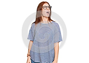 Young read head woman wearing casual clothes and glasses angry and mad screaming frustrated and furious, shouting with anger