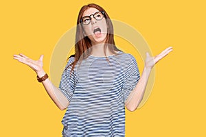 Young read head woman wearing casual clothes and glasses crazy and mad shouting and yelling with aggressive expression and arms