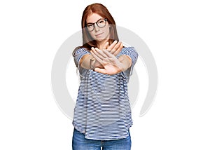 Young read head woman wearing casual clothes and glasses rejection expression crossing arms and palms doing negative sign, angry