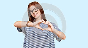 Young read head woman wearing casual clothes and glasses smiling in love doing heart symbol shape with hands