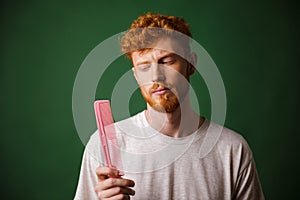 Young readhead beardy man looking at pink comb