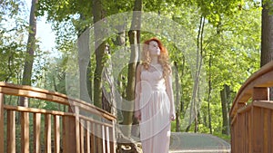 Young readhead girl walking in the park. Pretty caucasian woman in long light dress resting in the sunrays.