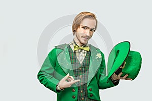 Young readhead man in green suit hold hat in hand and point on it. Guy look on camera seriously. on grey