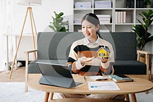 Young real estate agent worker working with laptop and tablet at table in home office and small house beside it