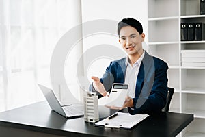 Young real estate agent worker working with laptop and tablet at table in modern office and small house beside it