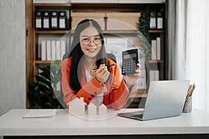 Young real estate agent worker working with laptop and tablet at table in office and small house beside it