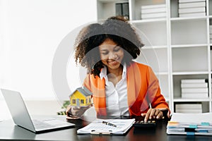 Young real estate agent worker working with laptop and tablet at table in office and small house beside it