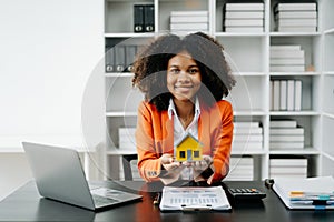 Young real estate agent worker working with laptop and tablet at table in office and small house beside it