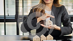 A young real estate officer or bank holding a small white house in the office. Home Loans, Dream Property Insurance and Real Estat