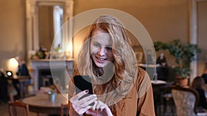 Young Red Hair Caucasian Woman Using Smart Phone Technology In Cafe