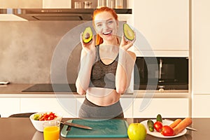 Young red hair woman smiles showing an avocado while preparing a snack in the kitchen