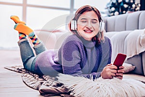 Young red-haired beaming girl in earphones relaxing at home