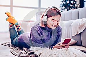 Young red-haired beaming girl in earphones smiling brightly