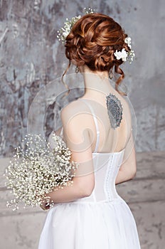 Young red-haired bride in elegant wedding dress. She stands with her back to the viewer.