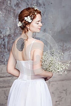 Young red-haired bride in elegant wedding dress. She stands with her back to the viewer. Her eyes are dreamy closed.