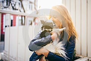 A young red-haired Caucasian woman holds a small funny dog in the arms of two colors of black and white chihuahua. Hugs and kisses