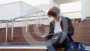 Young red -haired curly student sits on the stairs reads books in a university campus