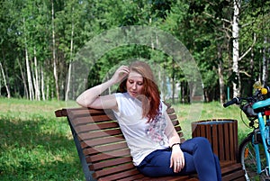 The young red-haired girl with bicycle sat down to have a rest on a shop and to do up let hair down.