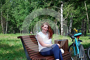 The young red-haired girl with bicycle sat down to have a rest on a shop and to do up let hair down.