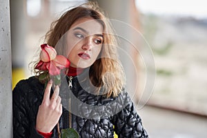 Young red-haired girl in a black jacket posing with a red rose in her hand