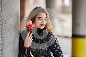 Young red-haired girl in a black jacket posing with a red rose in her hand