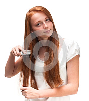 Young red-haired girl combing her long hair. Isolated on white b