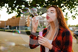 Young red haired girl in good mood blow air bubbles standing in the street