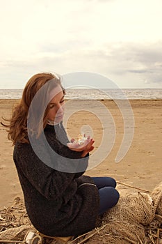 Young red-haired girl sits on a fishing net and looks at a seashell in her hands