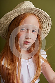 Young red-haired girl in a straw hat with long beautiful hair and big blue eyes. Hair the color of fire fluttering in the wind.