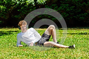 Young red-haired man in headphones lies on the green grass