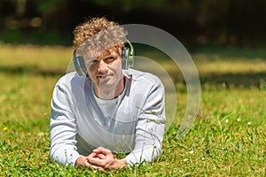 Young red-haired man in headphones lies on the green grass