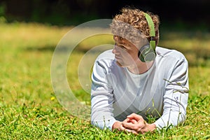 Young red-haired man in headphones lies on the green grass