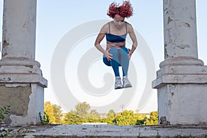 Young red-haired sportswoman jumping in the air. In a turquoise tracksuit, leggings, against the background of a