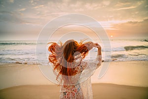 Young red-haired woman with flying hair on the ocean, rear view photo