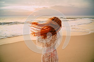 Young red-haired woman with flying hair on the ocean, rear view