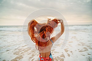 Young red-haired woman with flying hair on the ocean, rear view photo