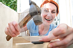Young red-haired woman hammering into a nail and smiling. The woman collects furniture in the apartment