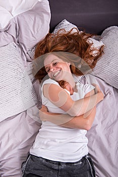 Young red-haired woman lying laughing in her bed