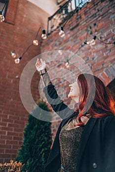 Young red haired woman pulling her hands to a light bulb. Success, idea, knowledge concept