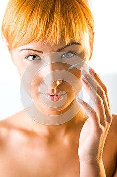 Young red-haired woman put cream on face