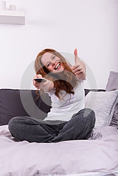 Young red-haired woman with the remote control in her hand watch